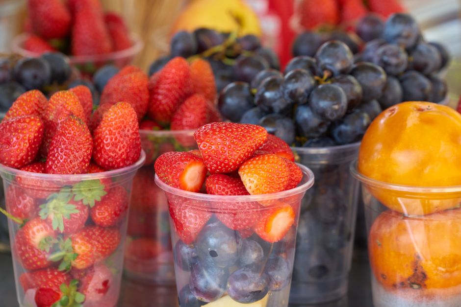 Vibrant strawberries, grapes, and persimmons displayed in plastic cups at a market.