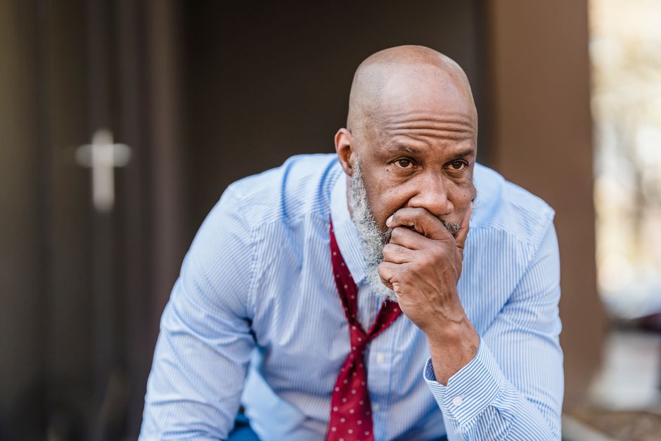 Unhappy bearded African American male worker in classy wear with hand on mouth looking away with concern while sitting on street