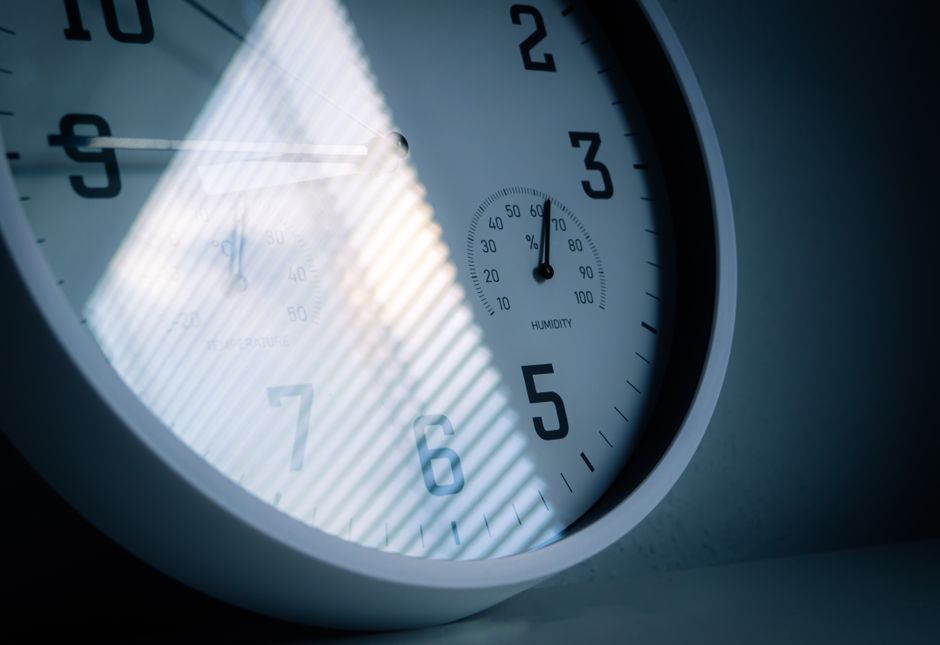 A close-up of a wall clock showing time and humidity, reflecting light and shadows.