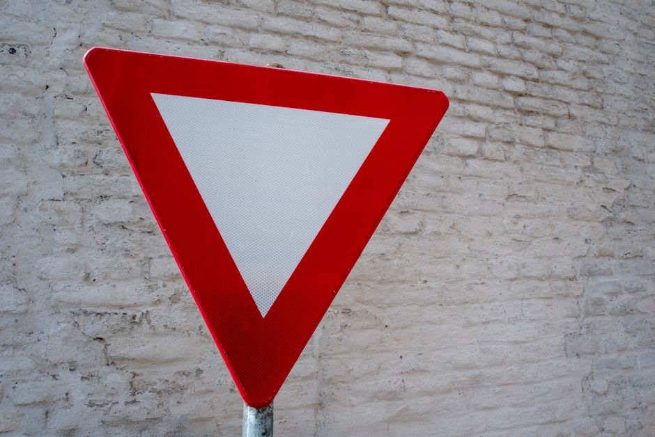 Close-up of red yield traffic sign against a textured white brick wall.