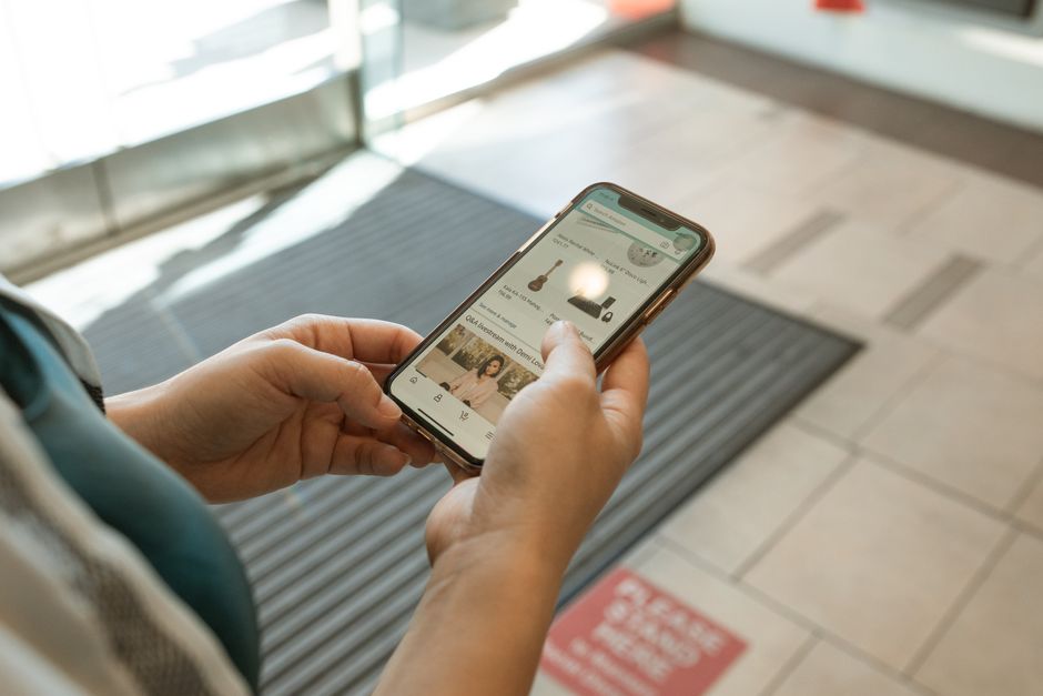 Close-up of hands holding a smartphone displaying an online shopping app in an indoor setting.