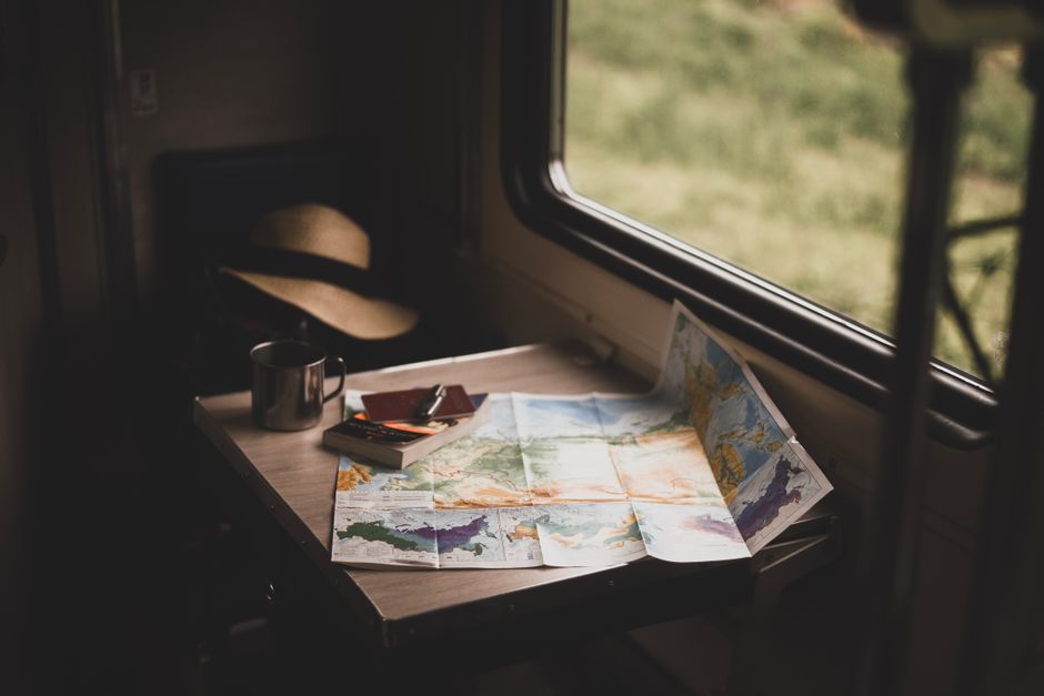A serene train ride setup with a world map, mug, and hat on a table, suggesting travel plans.