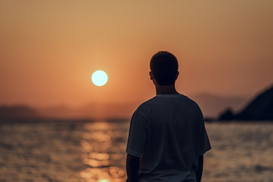 A man stands by the ocean observing a peaceful sunset, creating a serene silhouette against the sky.