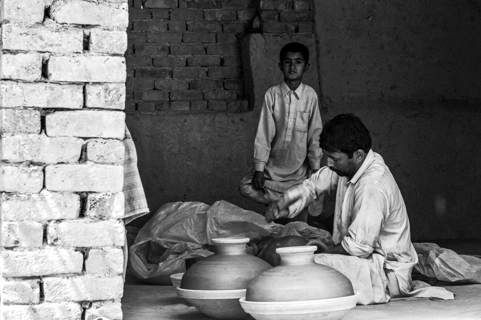 A father and son crafting traditional pottery inside a clay-brick building.