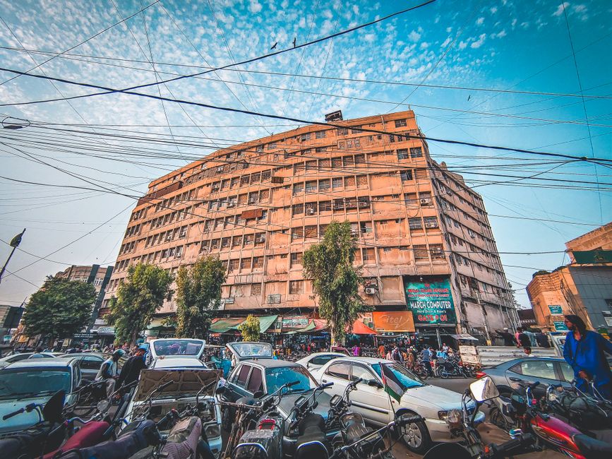 Wide-angle view of a busy street with an imposing apartment building and parked vehicles under a vibrant sky.