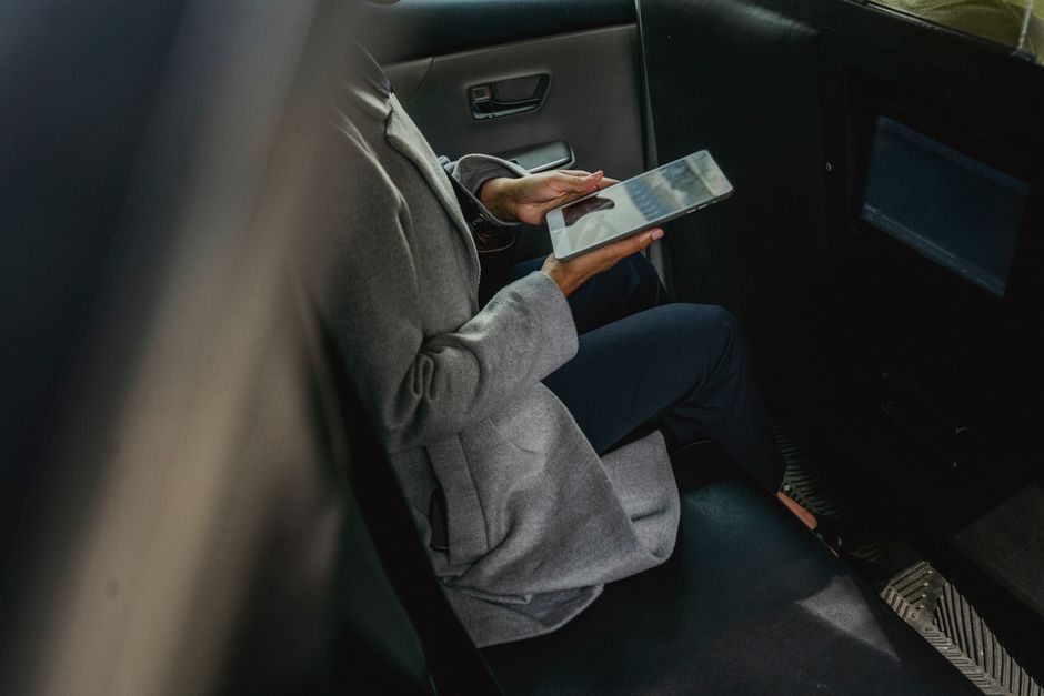 Crop unrecognizable female in casual clothes browsing tablet in backseat of modern cab