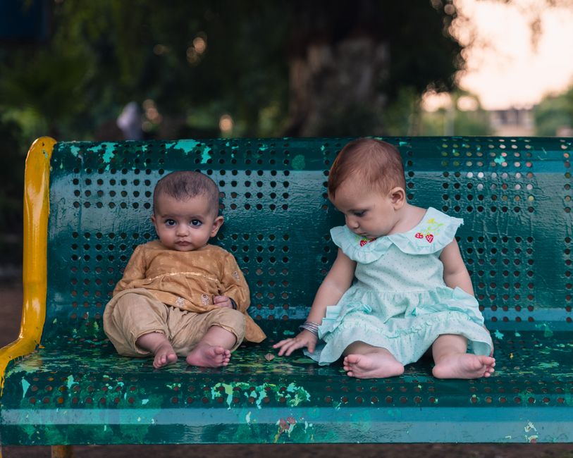 Two adorable babies sitting on a colorful park bench outdoors. Perfect for childcare and family themes.