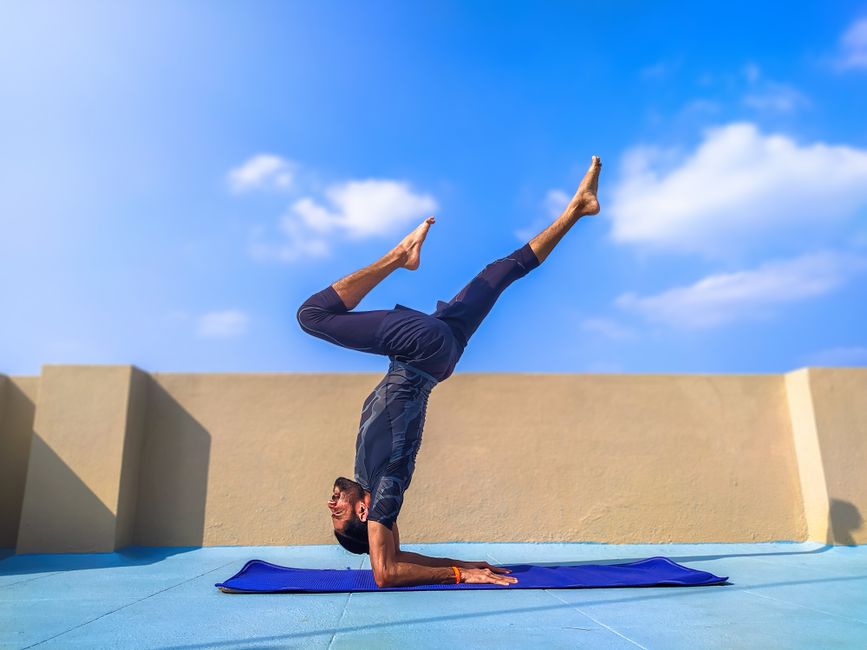 Adult man in yoga pose on rooftop with a bright blue sky background. Ideal for fitness content.