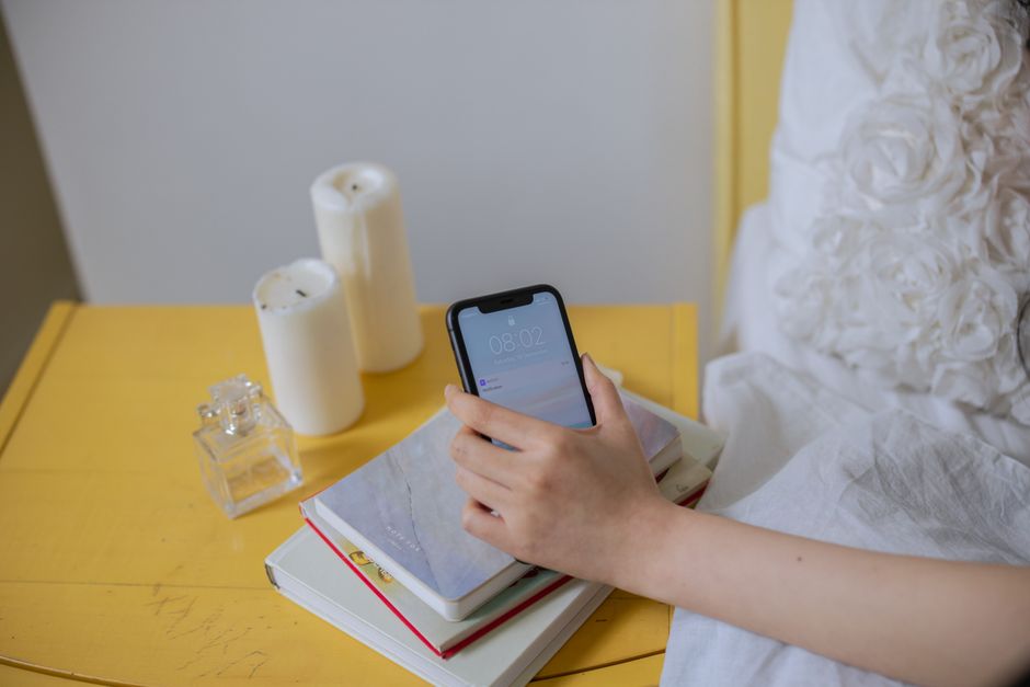 Hand holding smartphone over books on yellow table, perfect for cozy lifestyle themes.
