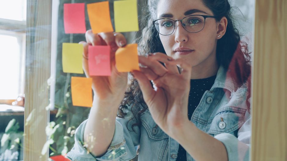 A woman organizing sticky notes on a glass wall in a modern office setting.