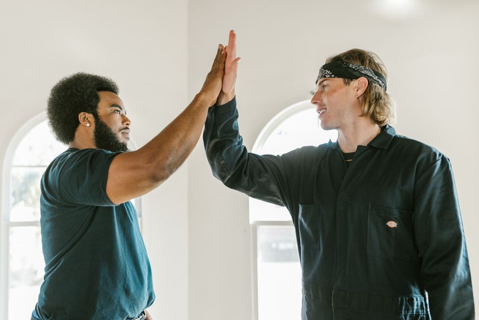 Two diverse colleagues high-five indoors, symbolizing teamwork and success.