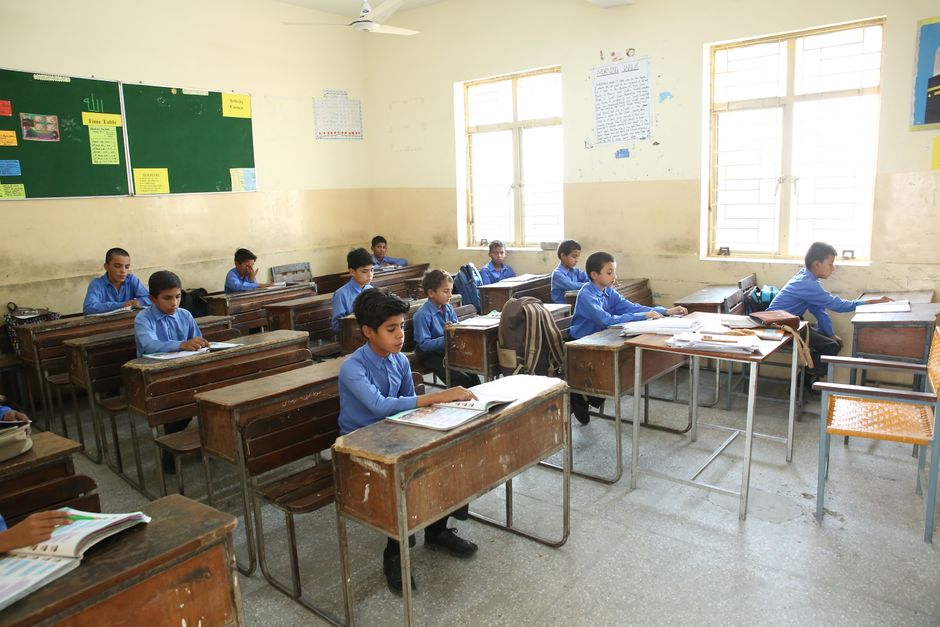 A group of young boys studying in a bright classroom filled with educational posters.