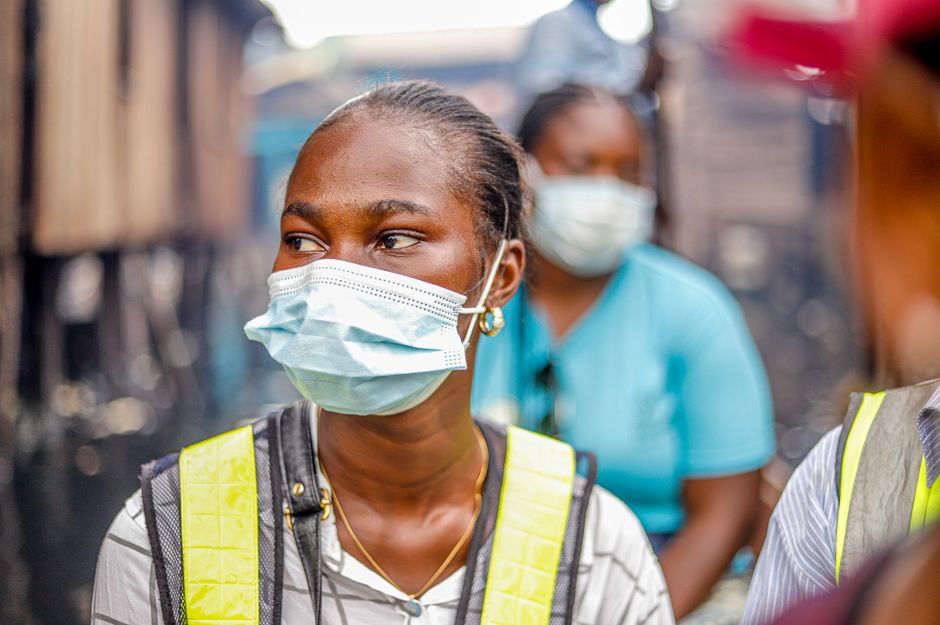 Women wearing protective masks and safety vests, working outdoors in urban setting.