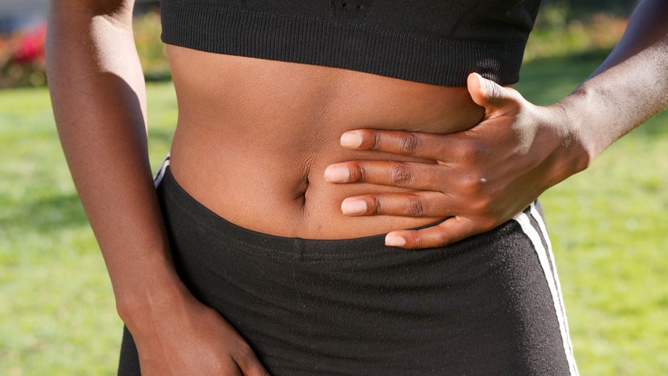 Close-up of a person holding their abdomen, indicating stomach discomfort, outdoors.