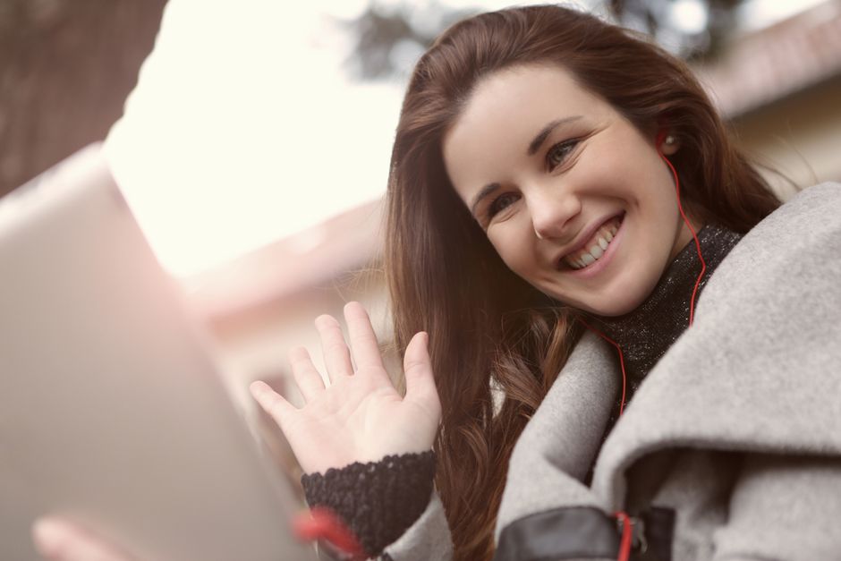 Young woman smiles and waves during an outdoor video call, showcasing modern wireless communication.