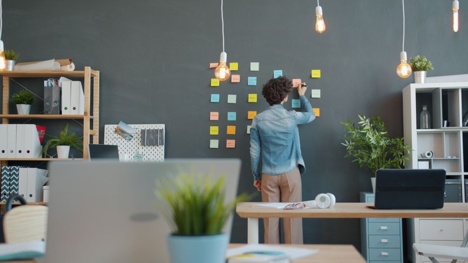 An adult writes on sticky notes during a brainstorming session in a modern office.