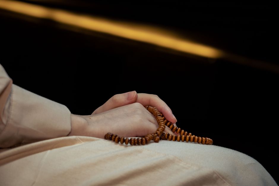 Hands holding wooden prayer beads against a black background, representing spirituality and meditation.