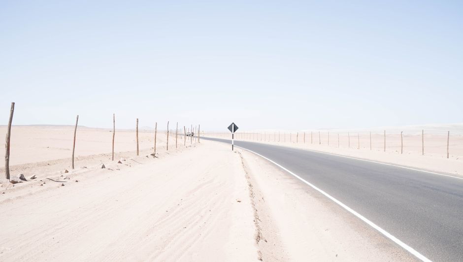 A deserted road winds through a vast, arid desert under a bright blue sky, capturing the essence of solitude and travel.
