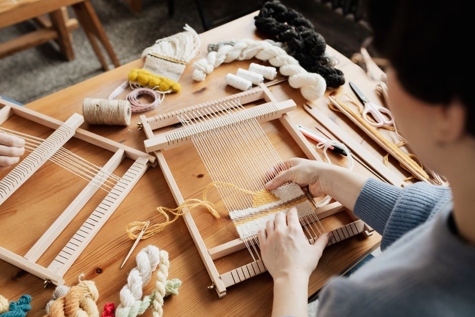 A person weaving textiles using a wooden hand loom, showcasing creativity and craftsmanship.
