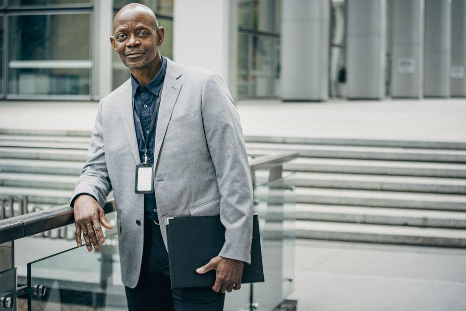Content adult African American male wearing classy formal suit standing with folder against modern business center and looking at camera