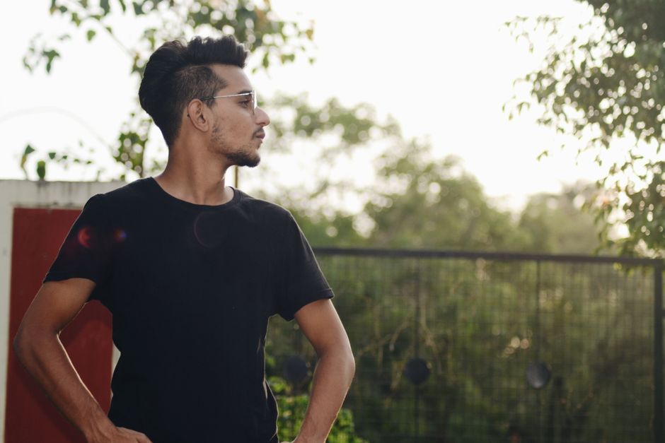 Stylish young man posing outdoors, wearing sunglasses and a black shirt, in a casual setting.