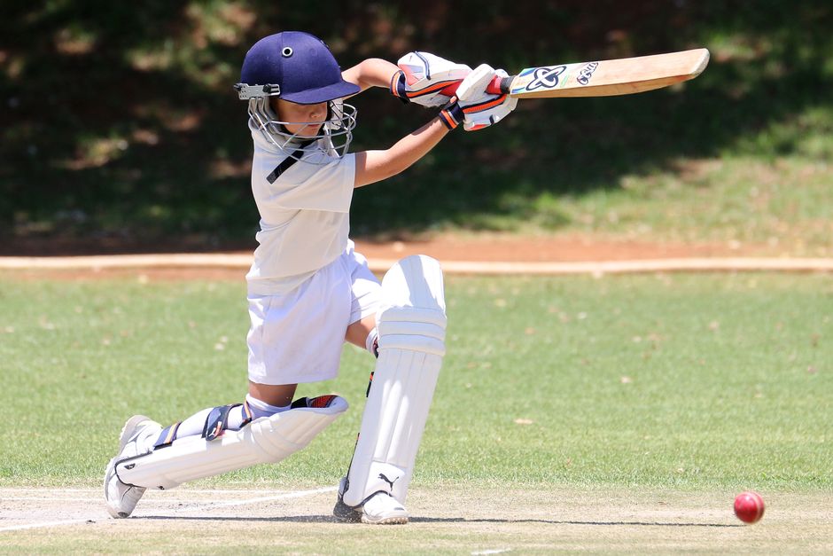 A young boy playing cricket, executing a classic sweep shot on a sunny day.