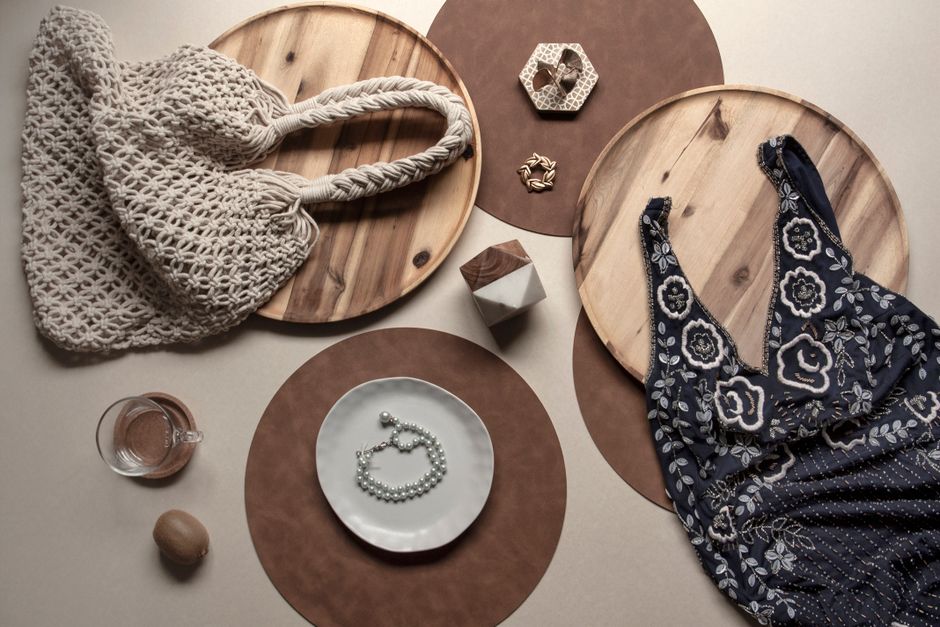 Flat lay of bohemian style accessories and attire including a bag, dress, and jewelry on rustic wooden surfaces.
