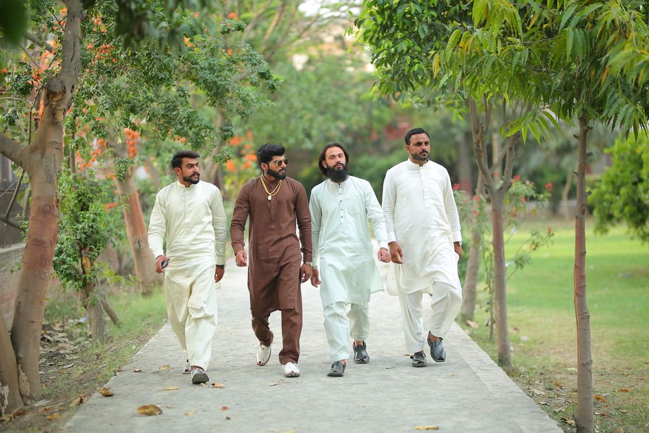 Group of men in traditional attire walking in a lush Lahore park.