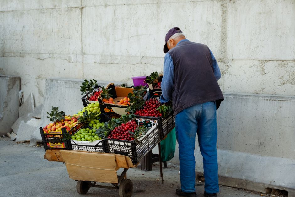 Elderly man selling fresh fruits and vegetables at an urban street market stall.