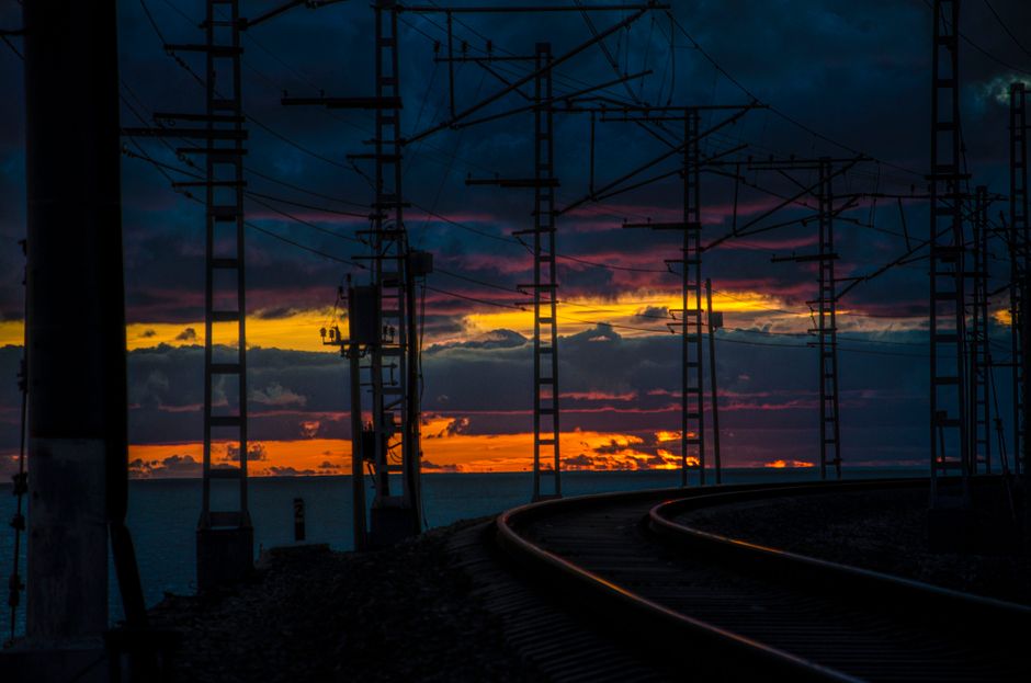 Silhouette of railway tracks against a vibrant sunset over the sea, creating a dramatic scene.