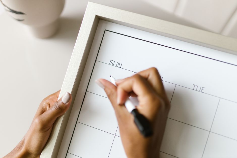 Hands holding a wall calendar, writing with a marker, organizing schedule.