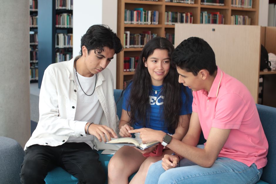 Three teenagers studying together in a library, engaged in a book discussion.