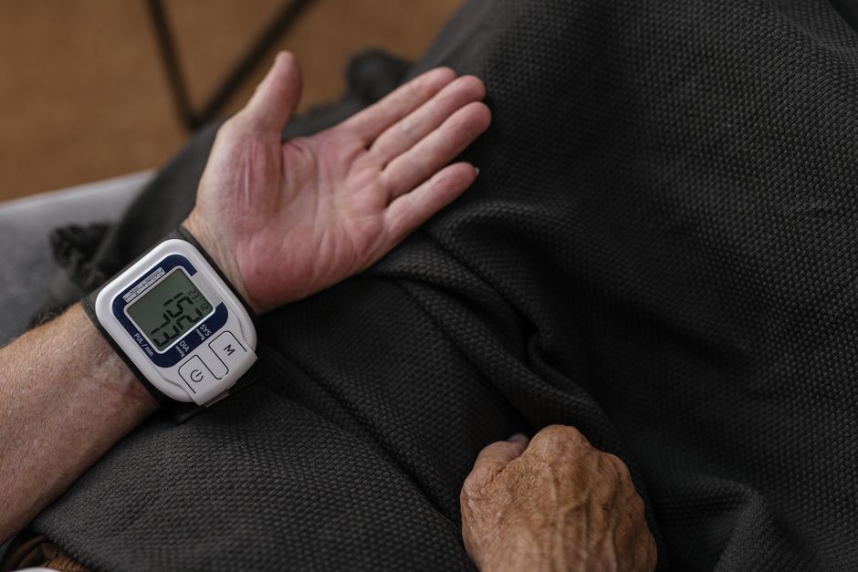 A senior adult using a wrist blood pressure monitor at home, focusing on health management.