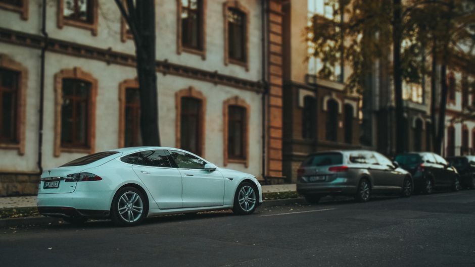 Side view of a sleek white sedan parked on a quiet urban street lined with trees.