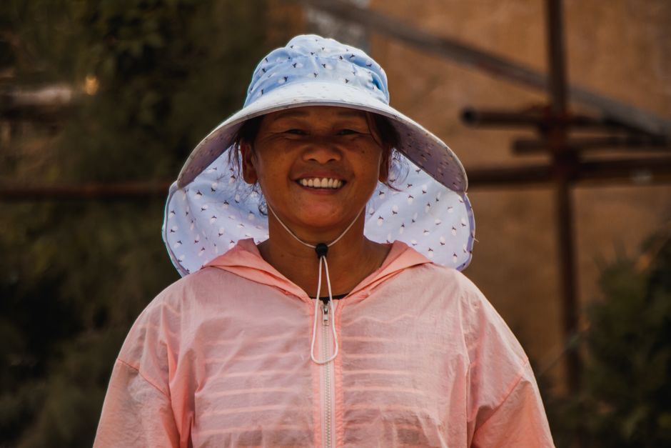 A cheerful woman wearing a sun hat and pink jacket, enjoying a sunny outdoors day.
