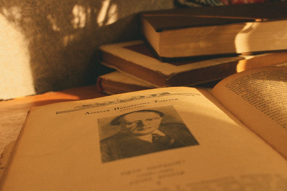 A stack of vintage books in warm sunlight with an open page displaying a portrait.