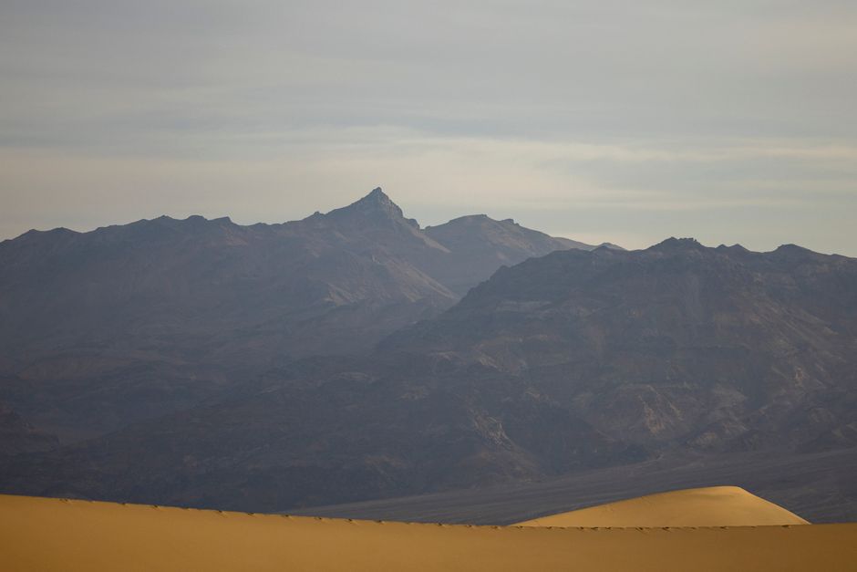 A tranquil view of mountains and dunes under a cloudy sky, showcasing natural beauty.