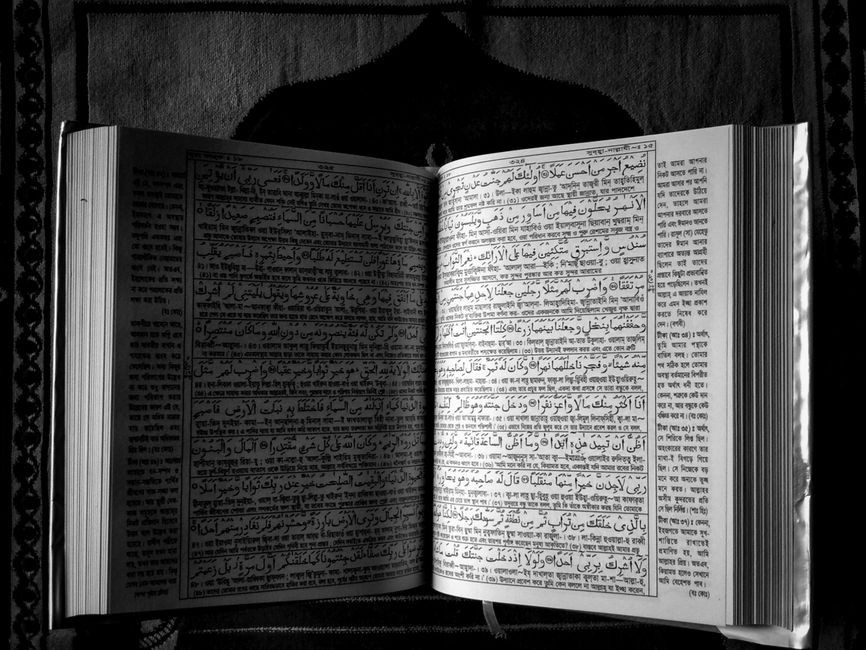 Black and white image of an open Quran illustrating religious texts in an artistic style.