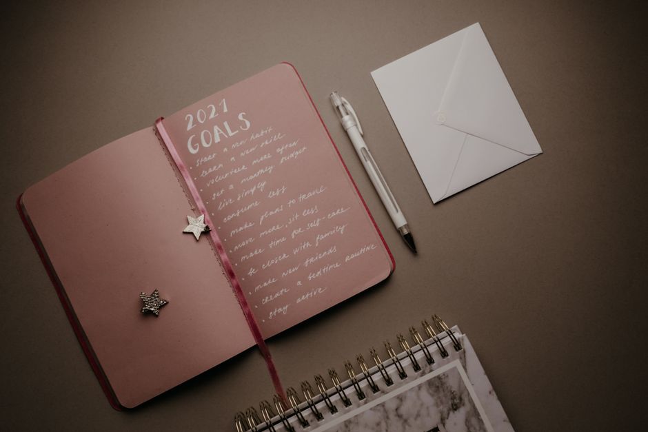 A flat lay image of an open journal with 2021 goals, pen, and envelope on a brown background.