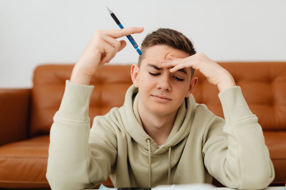 Online Gaming Effects on Students A stressed teenager in a hoodie struggles with homework, deep in thought indoors.