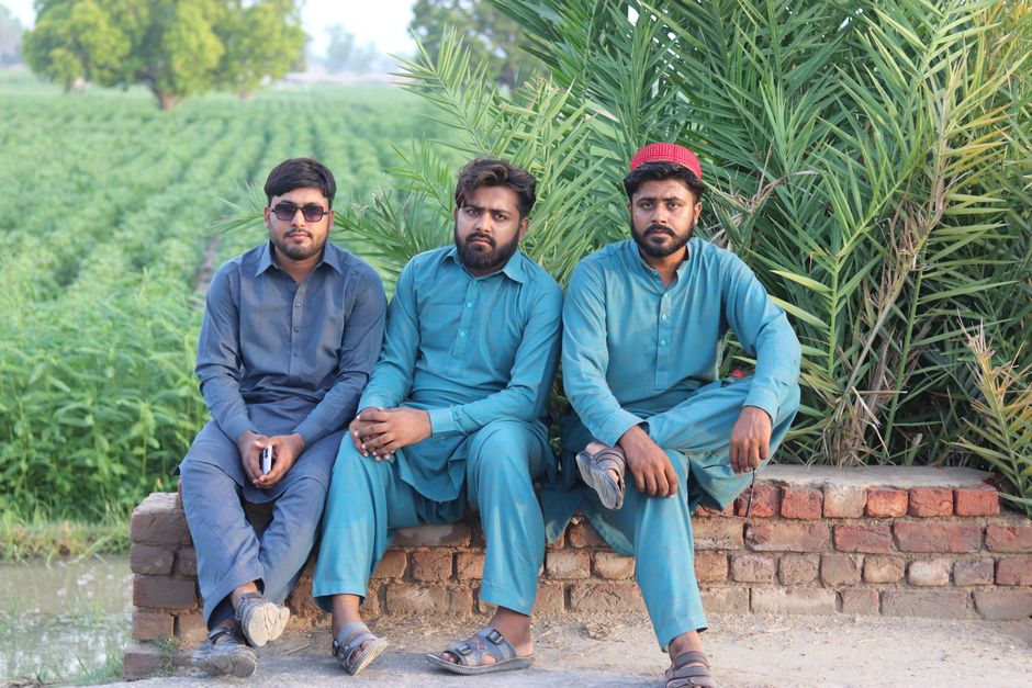 Three men in traditional attire sitting near a field, showcasing cultural lifestyle.