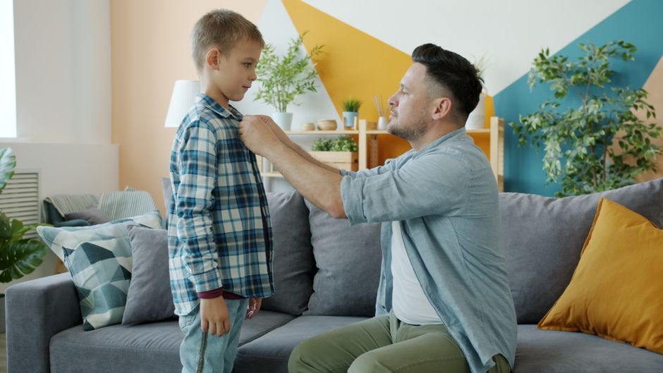 Father assisting son in fixing his shirt collar in a cozy living room setting.