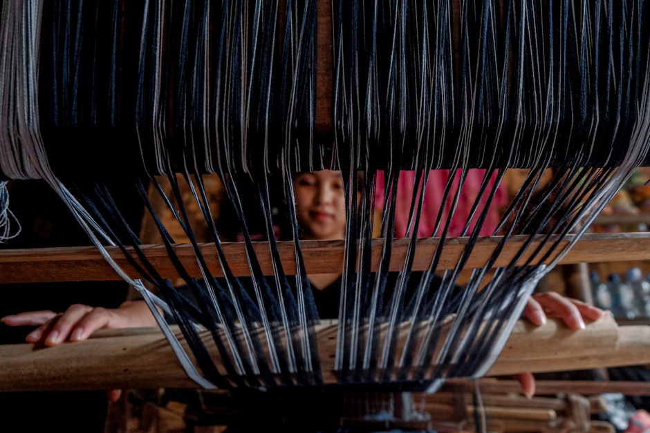 A woman skillfully weaving black and white threads on a traditional loom in an indoor setting.