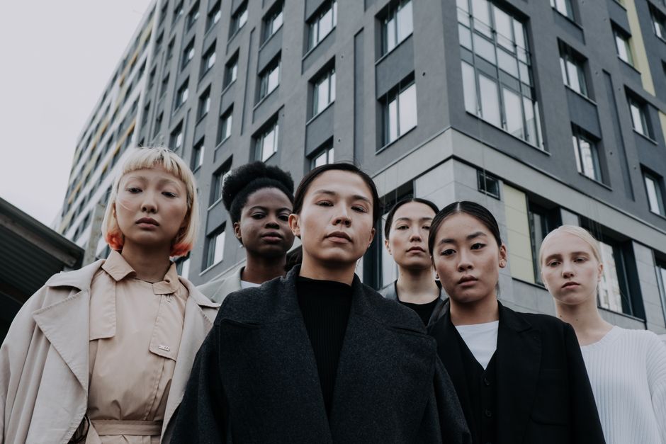 Strong and diverse group of women stand confidently in front of a modern apartment building.