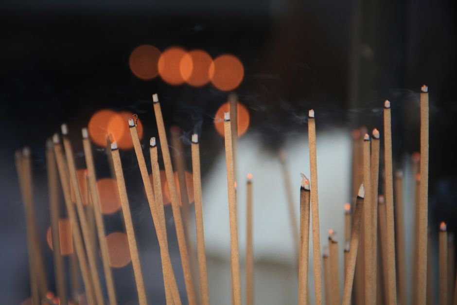 A tranquil image of multiple incense sticks with delicate smoke trails and warm bokeh lights.