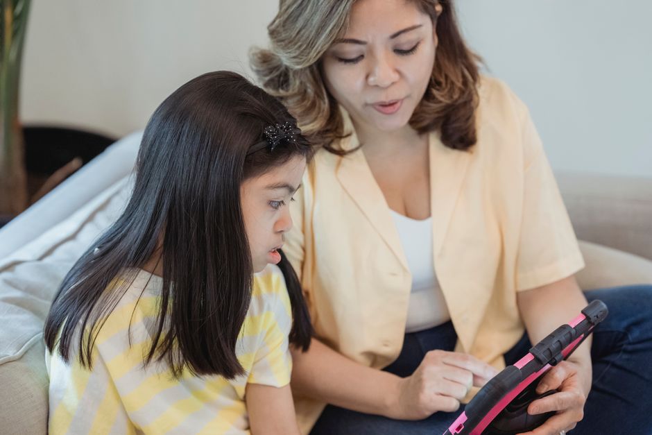 A mother and daughter engaged with a tablet, sitting on a couch, highlighting family bonding and technology.