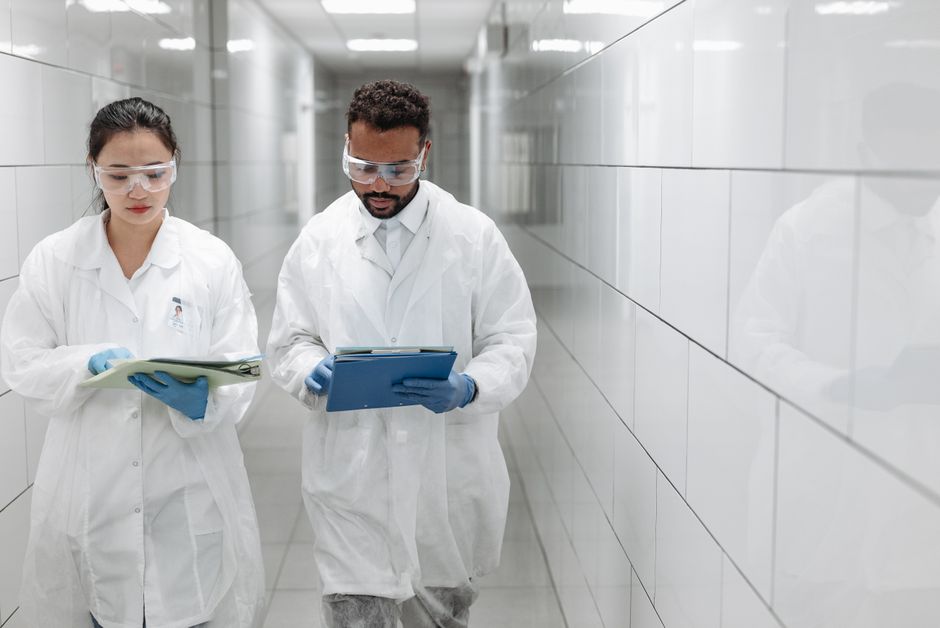Two researchers in lab coats review documents in a clinical laboratory hallway.