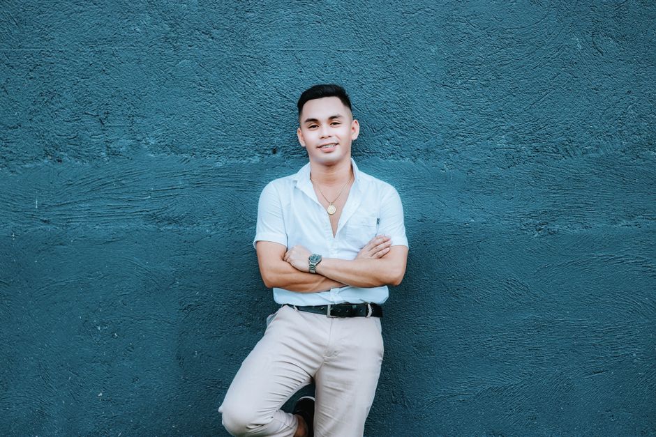 Smiling man in casual attire posing confidently against a blue wall.
