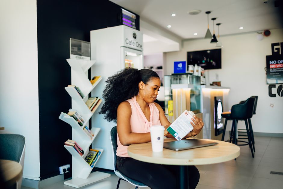 Black woman reading a book in a modern Lagos cafe, relaxed and focused atmosphere.