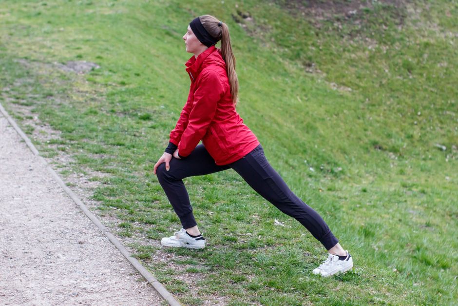 Woman in red jacket stretching in a park, illustrating outdoor fitness and healthy lifestyle.
